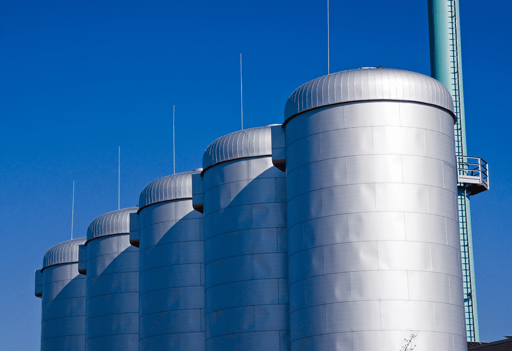 A row of silver IoT monitored industrial tanks against a blue sky.