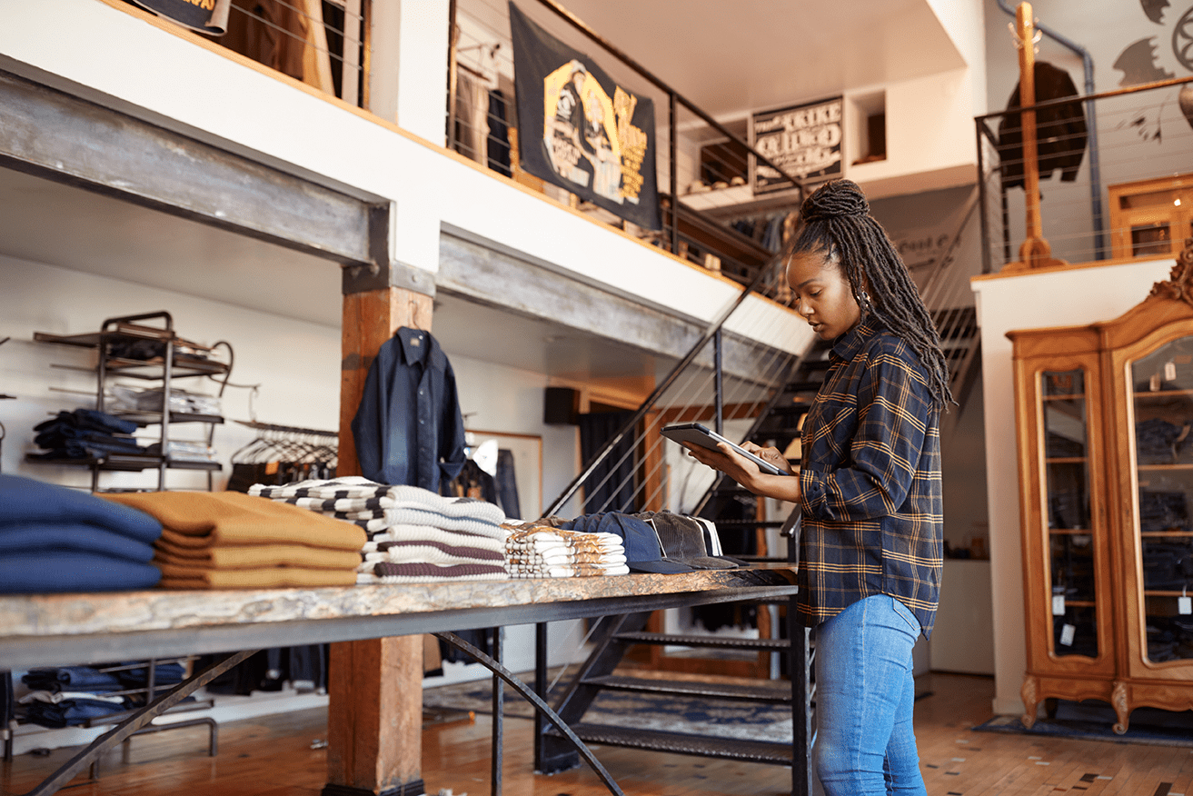 Retail Reinvented: Retail store owner using IoT-enabled tablet for inventory management in a modern boutique. Smart retail technology enhances efficiency by tracking stock levels in real-time. IoT solutions for retail improve supply chain visibility and streamline operations.